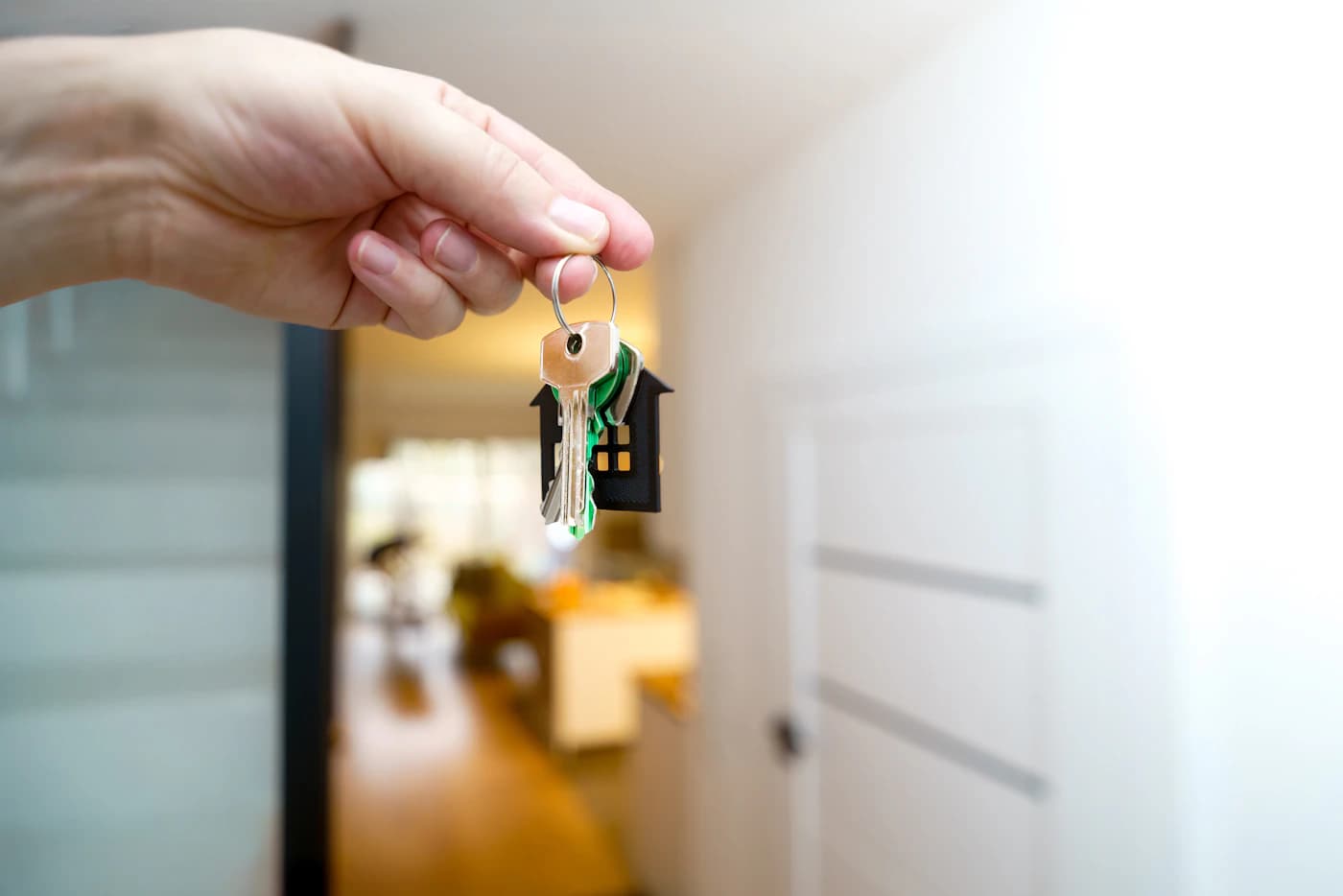 Una mano sostiene las llaves frente a la entrada de una vivienda.